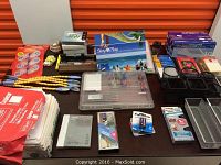 Photo of new and nearly new office supplies arranged on table, showing correction tapes, DVDs, hole punch, pens, stapler, organizers.