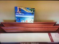Three wall shelves shown side by side: two brown wooden shelves placed on floor against wall with one white shelf still in original box visible in front.