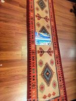 Full view of one Native area rug runner on hardwood floor, showing geometric and floral patterns with red border.