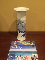 White porcelain vase approx 15 inches tall with blue floral painting, shown against beige background with brochure for scale.