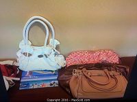 Seven assorted purses displayed together on a surface including a white leather D&G purse, a pink printed clutch, and multiple other colored handbags.