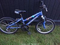 Side profile of blue Norco youth full suspension mountain bike on grass showing frame, wheels, drivetrain.
