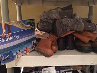 Shelf filled with multiple pairs of brown and black leather boots, some lined with fur, size 8, including moccasins and hiking boots.