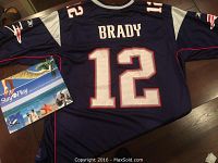Back of the navy blue Tom Brady Patriots jersey showing name and number 12 details with tags attached and laid on wooden surface.