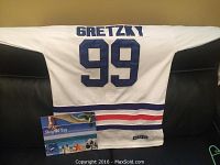Back view of the authentic Wayne Gretzky Edmonton Oilers jersey showing name and number 99 in blue on white fabric with stripes and attached promotional item.