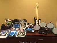 Full view of the lot on a wooden surface showing consoles, dance pads, Rock Band instruments, game discs, and accessories.