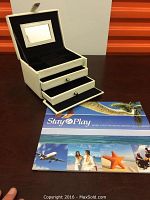 White leather jewelry box closed and atop surface with brochure showing size comparison