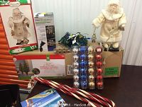 Overview photo showing all items in the lot including the pre-lit tree box, Santa figures, ornaments, string lights and candy cane decorations on the table.