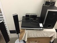 Full view of Sony surround sound system showing four tall slimline speakers, central horizontal speaker, subwoofer, and DVD player with amp unit.