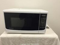Front view of white Danby microwave showing black door, control keypad on right and power cord visible at the side.