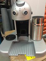 Front view showing the silver machine front panel with two control dials and milk frother jug attached on right.