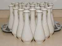 Front angled view of 24 off-white ceramic vases grouped closely together on a silver tray, showing their shape and speckled finish