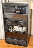 Full front view of a black metal wheeled audio equipment rack with five stacked components: mixer, equalizer, Sony dual cassette player, and two amplifiers.