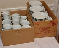 Two cardboard boxes filled with stacked flowered plates and cups.