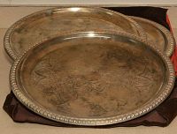 Six silver-plated serving trays stacked, showing tarnishing and some rust, with a decorative scalloped bead edge design. Stored in a dark fabric pouch.
