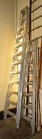 Photo showing a leaning aluminum 8-step stepladder with visible side rails and steps, placed indoors beside other ladders.