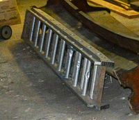 Metal extension ladder lying horizontally on a concrete floor. Shows cylindrical metal rungs and metal side rails. Ladder is in folded shorter length corresponding to 9 rungs visible.