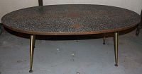 Full table showing oval shape, mosaic tabletop with a black and grey speckled pattern, and four brass tapered legs