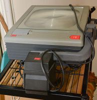 Photo of 3M 8200S overhead projector showing top glass surface, lamp housing with cord, and black metal trolley.