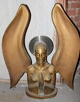 Metal sculpture of a praying angel with large upward wings and a halo-like disc behind the head, brass-colored finish, shown against neutral background.