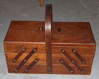 Closed view of wood sewing box with handle and metal supports on layered sides.