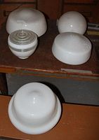 Five white opaque glass globe light covers arranged on a wooden surface, showing different sizes and shapes with the round openings visible.