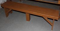 Wooden bench with brown finish showing wear including nicks and scratches on surface, photographed on concrete floor.