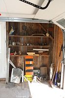 Overview of wooden shelving with various items including wood clamps, weights, stove, fire extinguisher, and signs.