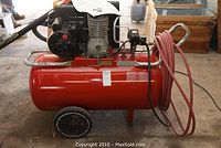Side view of the red compressor tank with attached wheels, handle and coiled red hose