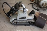 Rockwell belt sander with dust collection bag and sanding belts laid out on the ground
