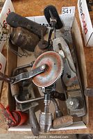 Vintage woodworking and hand tools arranged in a box showing a Stanley plane, shoulder brace, oilers, and other tools.