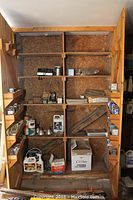 Wooden cupboard with multiple shelves holding various supplies including boxes of screws and hardware, cans and bottles at bottom shelves.