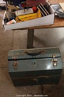 Photo of the toolbox closed from above with an open storage box on a table showing various bits and tools including drill bits, hole saws, wood bits, and other small tools.