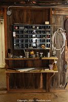 Wide view of metal organizer bin hung on wall containing assorted nuts, bolts, and hardware. Wooden shelves below holding more hardware items.