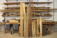 Overall view of metal rack and floor stacked with various boards and firewood under table