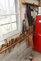 Window-side view of tool rack showing chisel handles and partial saw handles on wooden rail above block wall