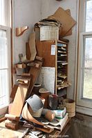 Wooden shelving rack filled with sandpaper sheets, discs, rolls, and blocks positioned by windows