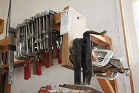 F-type clamps mounted on a wooden rack with red handles and some metal clamps attached on the side. Shows overall view of clamps.