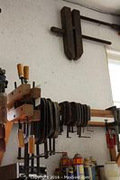 C clamps and wood clamps hanging on wooden rack, showing size variety and wear.