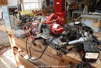 Power tools arranged on workbench showing Milwaukee circular saw, Rockwell router, Shopmate Sabre saw, Black & Decker drill, soldering stand, and boxed Craftsman spray gun.