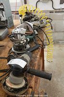 Porter Cable grinder and assorted power tools lined on bench including router, jigsaw, polisher, drill, with coil hose in background