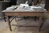 Front angle view of old solid wood table with worn finish and various documents on top