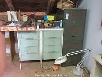Photo showing two metal-framed cabinets with wood drawers, metal 4-drawer filing cabinet, miscellaneous contents on top, and weighted base work light on the floor.