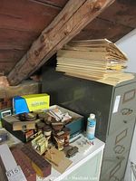 Photo shows a filing cabinet with folders on top, yellow Clarks box, round tins, a bottle of modeling thinner, and small parts scattered on a tabletop.