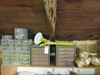 Wide view showing all storage bins including two metal five-drawer bins, multiple clear plastic organizer bins on the left, large plastic bin behind packed parts, and the yellow adjustable work light on top.