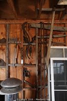 Wide shot of wooden wall with old farm tools hanging, including long handled pitch fork, pulleys, rails, and yoke pieces