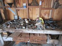 Wide photo of wooden bench holding assorted marine parts including transom handles, shackles, cables, and various hardware with wooden planks stored underneath.
