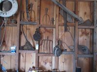 Overall wall-mounted display of various farm implement heads and pulleys hung on wooden boards