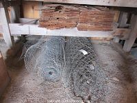 Rolls of wire fencing and bundles of cedar shingles stored on the ground and shelving.
