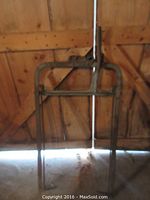 Full view of the old metal hay fork showing its full length and frame against wooden barn door.